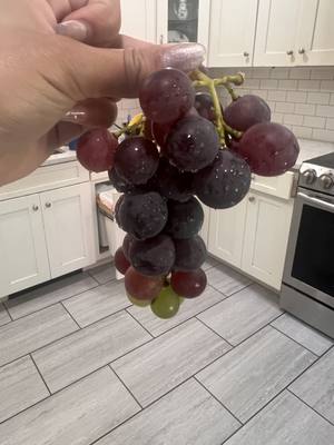A full bunch of dark purple-red grapes held up in the kitchen